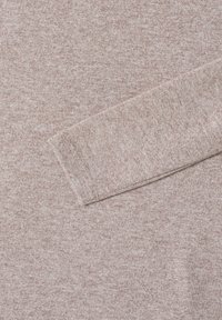 Tissu texturé brun clair avec un motif subtil chiné, présentant des manches longues. Le matériau semble doux et tricoté.
