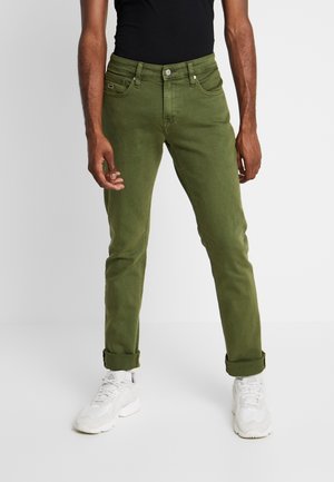 Jeans en coton verts avec une coupe slim, comportant cinq poches, une fermeture par bouton et des poignets roulés. Associés à des baskets blanches.