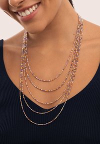 Wielowarstwowy naszyjnik z koralików w kolorach fioletowym, pomarańczowym i złotym, o gładkiej fakturze i różnych długościach, noszony na ciemnym topie.