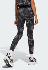 Leggings de estampado floral negro, confeccionados en tejido elástico, con una cintura alta y una silueta ajustada, combinados con zapatillas blancas y negras.