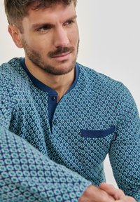 Camisa de manga larga en azul con un patrón geométrico, cuello en contraste de color azul marino, tapeta de botones y un bolsillo en el lado izquierdo del pecho.
