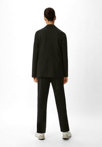 Schwarzer maßgeschneiderter Anzug mit einem langen Blazer und geraden Hosen. Der Stoff wirkt glatt mit minimal sichtbaren Nähten und ohne Muster.