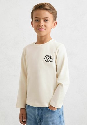 Kremowa koszula z długim rękawem o fakturowanym wykończeniu, z czarnym haftowanym logo na piersi i okrągłym dekoltem.