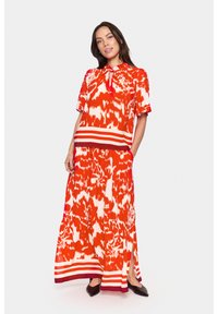 Abito maxi con un vivace motivo rosso e bianco, maniche corte, collo con lacci, vita elastica e orlo a righe orizzontali. Tessuto liscio, vestibilità comoda.