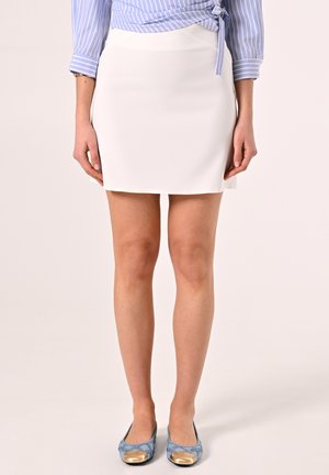 Jupe mini blanche avec une texture lisse et un design ajusté, associée à des ballerines bleues à motifs avec des accents dorés à la pointe.