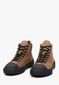Tan suède hoge schoenen met een zwarte rubberen neuskap, zwarte veters en een ritssluiting aan de zijkant; platte rubberen zool met een geribbelde grip.