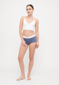 Hvit bomull bralette med tynne stropper, parret med blåstripete boxershorts med hvit elastisk midje. Glatt tekstur, uformell stil.