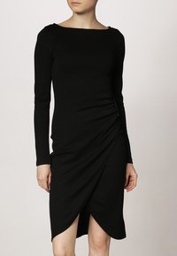 Černé dlouhé šaty s dlouhým rukávem z elastického materiálu, s lodičkovým výstřihem a nařaseným designem s asymetrickým lemem.