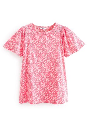 Blouse rose à manches courtes avec un petit motif floral blanc et des plis subtils près de l'encolure arrondie.