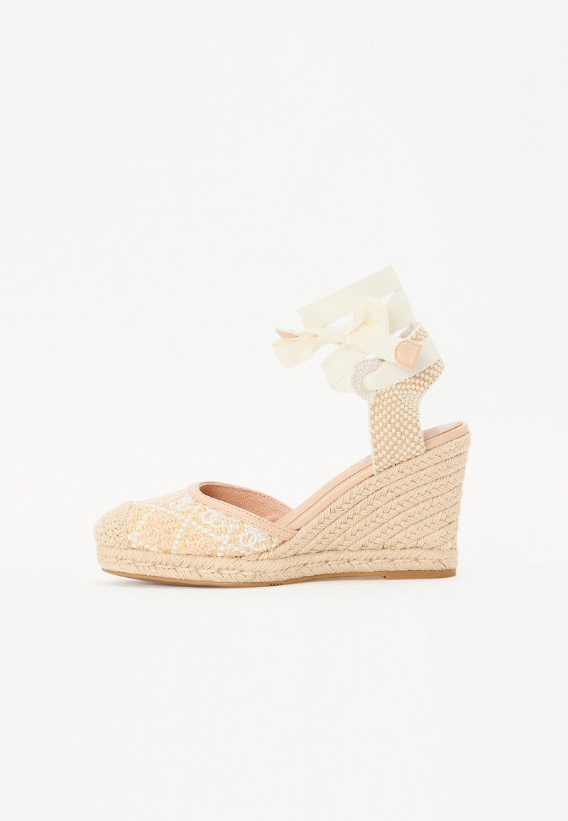 Espadrille à semelle compensée en tissu tissé texturé de couleur beige clair, avec un bout ouvert et des brides croisées à la cheville.