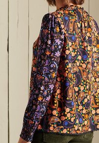 Langarmblouse van donker stof met een levendig, gekleurd paisley- en bloemenpatroon; gathered schouders en knoopmanchetten.