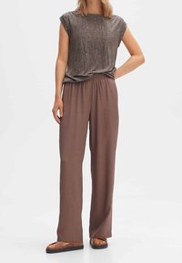 Lichte, getextureerde bruine top met korte mouwen, gecombineerd met ruime, vloeiende bruine broek met een elastische tailleband en platte sandalen.