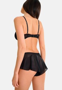 Soutien-gorge noir et jupe en maille évasée avec un léger éclat. Bretelles ajustables, dentelle sur le soutien-gorge et détail en volants superposés sur la jupe.