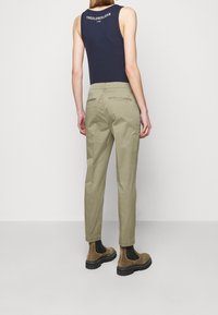 Ljust olivgrön bomullstrouser med tapered fit, med två bakfickor och sömdetaljer. Bärs tillsammans med en marinblå tanktop och bruna chelsea-boots.