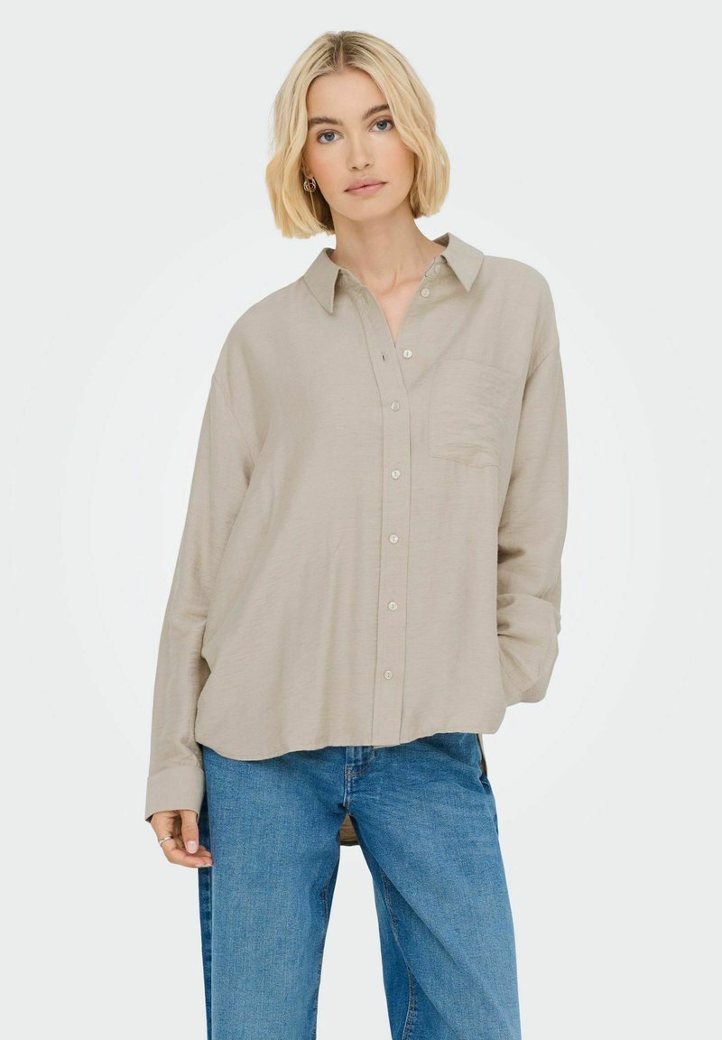 Lichtbeige oversized knopenoverhemd met lange mouwen en een zak. Gecombineerd met blauwe jeans, met een ontspannen pasvorm. Glad textuur.