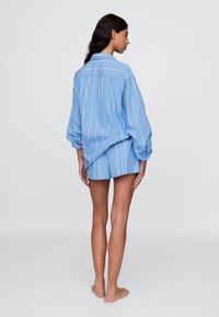 Camisa de rayas azul claro y pantalones cortos a juego. La camisa tiene un corte relajado con mangas largas y cuello abotonado. Textura suave de algodón.