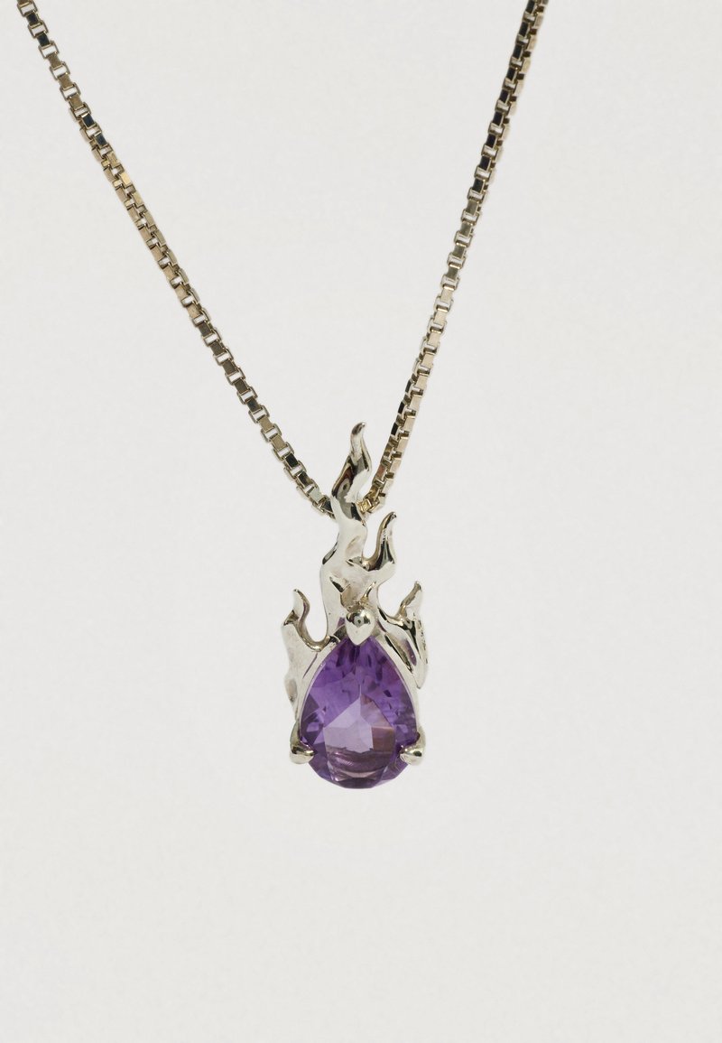 Srebrny wisiorek w kształcie płomienia, trzymający fasetowany, łezkowaty fioletowy kamień szlachetny na srebrnym łańcuszku.
