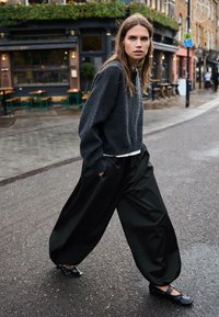 Túlméretezett szürke pulóver és bő fekete nadrág, fekete cipővel párosítva, egy nedves utcán sétálva, közel a kültéri kávézó üléseihez.