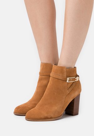 Suede-Ankle Boots in Beige mit einer strukturierten Oberfläche, ausgestattet mit einem Schnallenakzent und einem gestapelten Holzabsatz. Runde Zehenform.