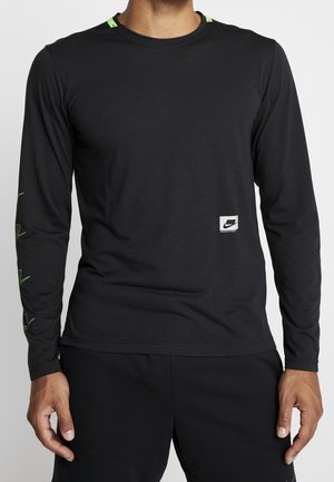 Mand iført sort langærmet Nike-shirt med lille logo på brystet og neon-grønne grafiske detaljer på ærmer og skuldre.