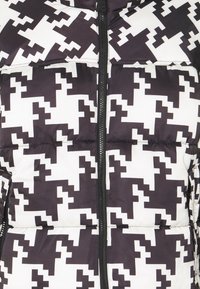 Puffjacka med ett geometriskt mönster i svart och vitt. Har dragkedjestängning och vadderad yta som ger isolering och värme.
