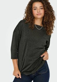 Sort, top med trekvartærmer i en glitrende tekstur, løs pasform og rund halsudskæring; parret med mørkeblå jeans.