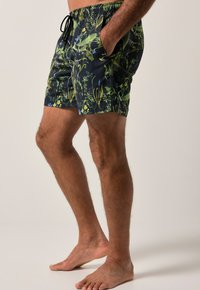 Costumi da bagno di colore blu scuro con vivaci motivi floreali verdi e blu. Presentano una vita elasticizzata con cordino e due tasche laterali.