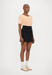 Perzikgestreepte gebreide top, hoog-wijde zwarte rok met zakken en crèmekleurige sneakers met gekleurde strepen. Korte mouwen en casual fit.