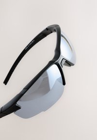 Melni saulesbrilles ar gludu dizainu, spoguļotu stiklu un fakturētām gumijas kājiņām. Rāmim ir leņķiskas līnijas un spīdīga apdare.