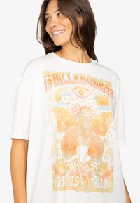 Camiseta blanca oversized con gráficos de mariposas coloridas y esqueletos, con texto y motivos naturales en tonos naranja, amarillo y pasteles.