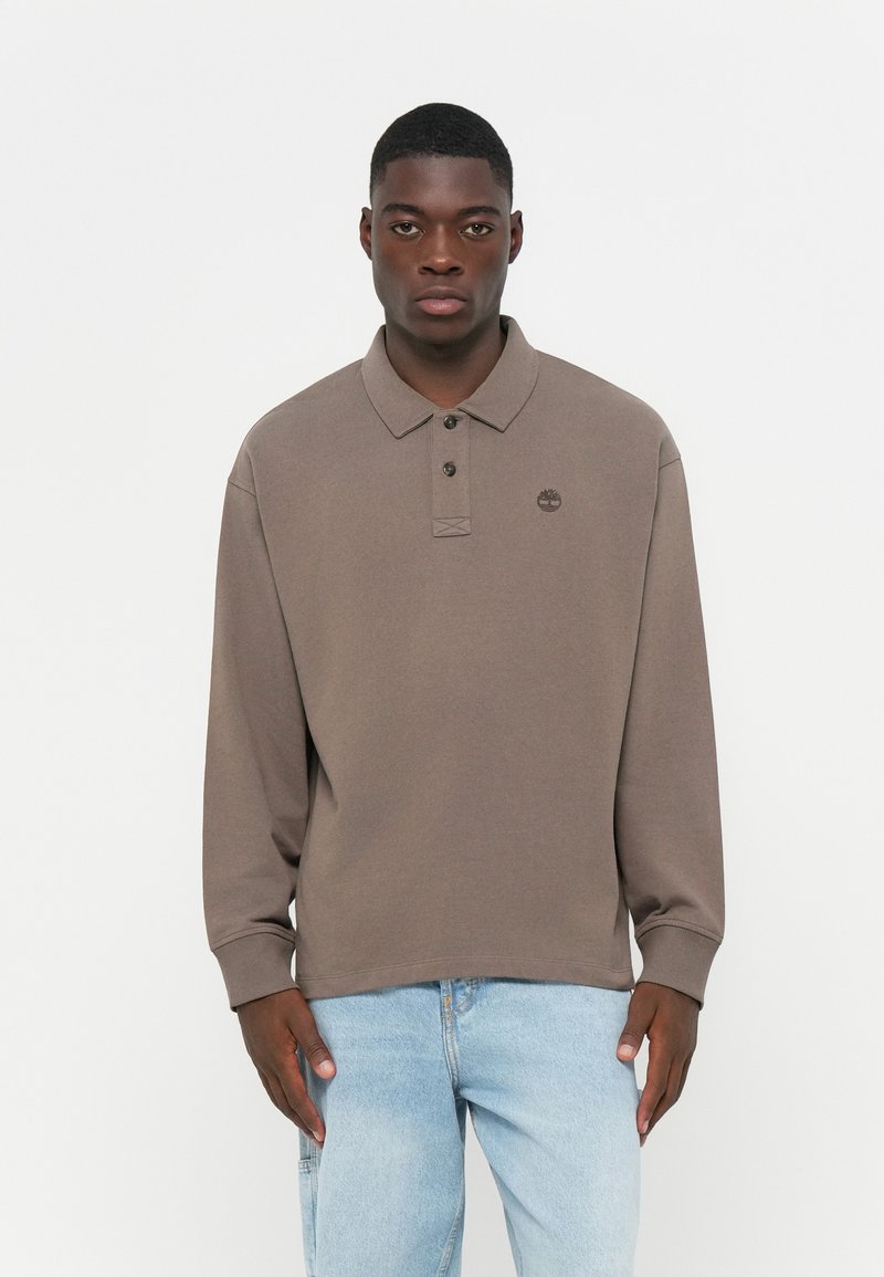 Brown long-sleeve polo shirt with a buttoned collar and a small logo on the chest. Fabric appears soft with a solid color and relaxed fit.