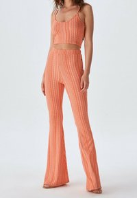 Perzikkleurige bijpassende crop top en uitlopende broek met verticale gestreepte patronen en een gestructureerde afwerking. De bandjes op de top zijn dun.