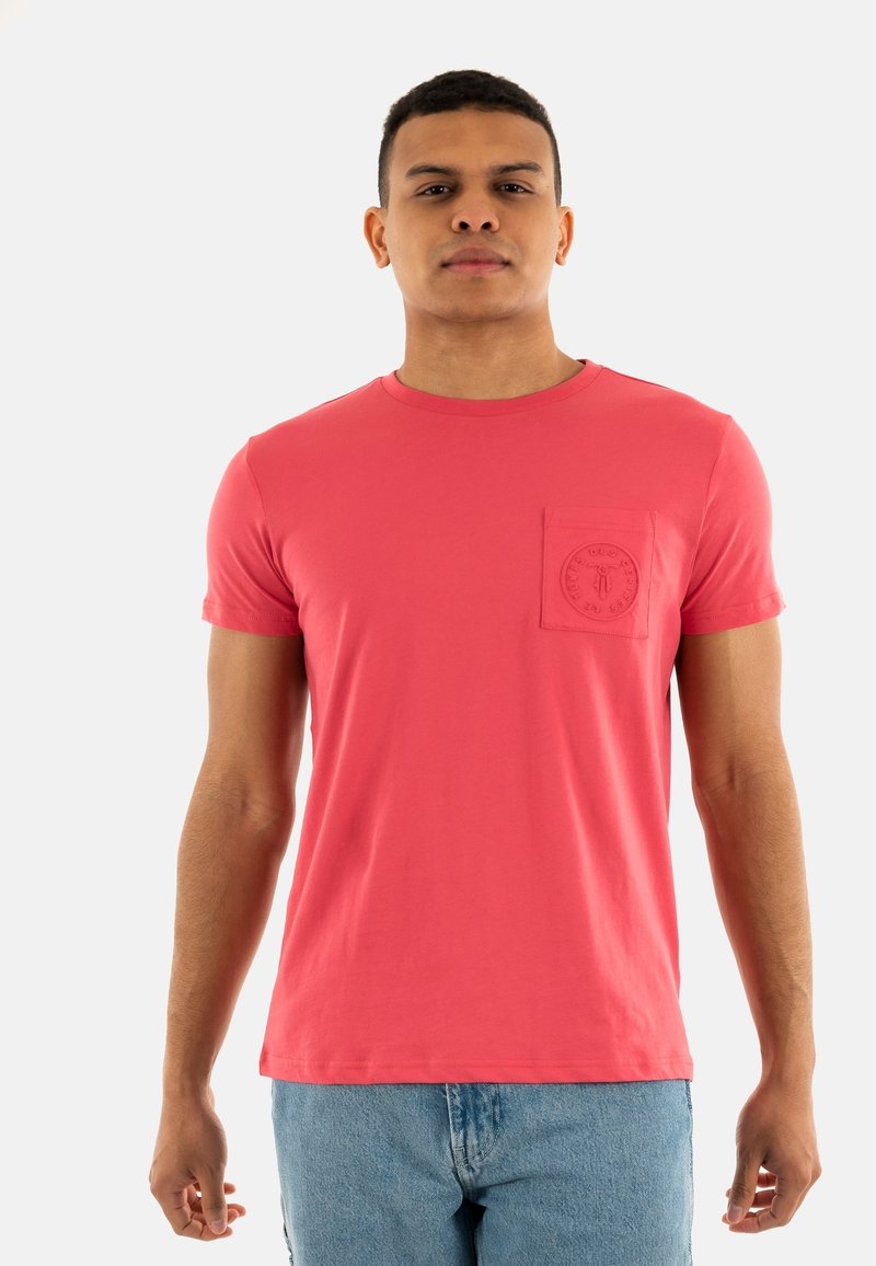 T-shirt à manches courtes et col rond en corail rose, avec une poche texturée et un détail de logo circulaire. Fabriqué en coton doux.