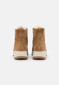 Brązowe zamszowe botki za kostkę z miękkim futerkiem z materiału syntetycznego, z suwakiem po boku i teksturowaną gumową podeszwą dla lepszej przyczepności.