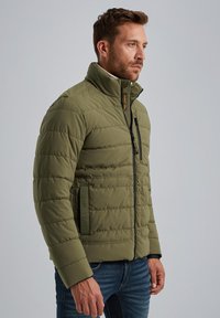 Olive green puffer jacket with horizontal quilting, high collar, zip closure, front zipper pocket, and embossed logo on the side.
