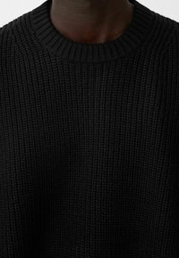 Pull noir en maille avec un col rond, des côtes texturées et une coupe ample, mettant en avant un tissu doux et épais.