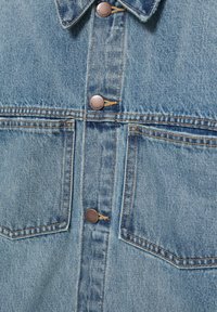 Lyseblå denimjakke foran med to brystlommer, brun syning og metal knapper indgraveret med "PULL&BEAR."