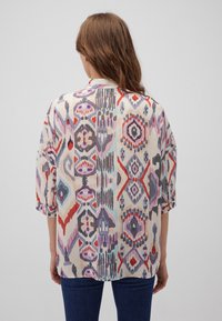 Loose-fit blouse with a colorful, abstract print. Features a soft fabric, short sleeves, and a round neckline. Colors include purple, red, and blue.