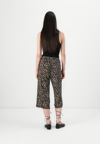 Pantalons larges à imprimé léopard avec une coupe décontractée, dotés d'une taille élastique et d'une longueur cropped, accompagnés de ballerines noires à lacets.
