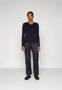 Pikkade varrukatega must pluus kombineeritud tekstuuriga tumeda halli pükstega, millel on logo; mõlemad esemed on valmistatud venivast ja hingavast materjalist.