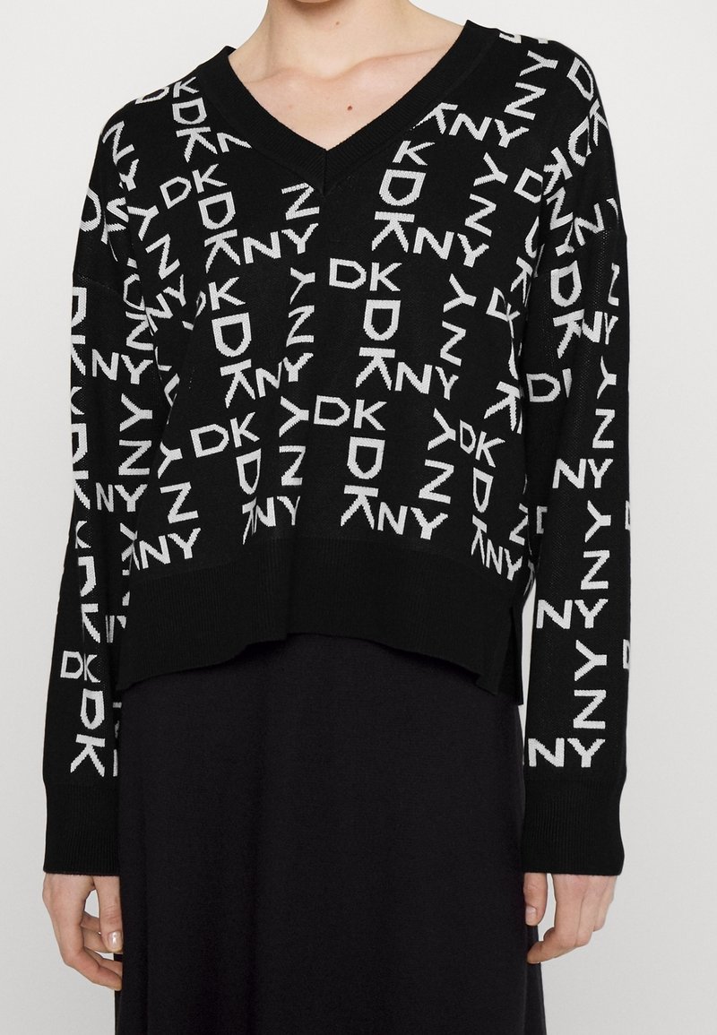 Musta neulepaita, jossa on V-pääntie, ja joka esittelee toistuvaa valkoista "DKNY"-logoa. Laajentuva helma ja pitkät hihat, joissa on ribbireunat.