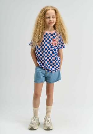 Blå og lyserød ternet t-shirt med "SELF LOVE CLUB" tryk, parret med lyse denim shorts. Stylet med beige stribede sokker og sneakers.