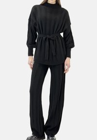 Ensemble deux pièces noir en maille avec manches longues, texture côtelée et ceinture à nouer. Le haut présente un col montant, le pantalon a une coupe pantalon large.