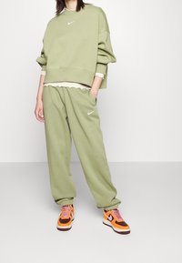 Olivgrön oversized sweatshirt och matchande joggers med en vit Nike-logga. Ett par livfulla sneakers i orange och vinröd.