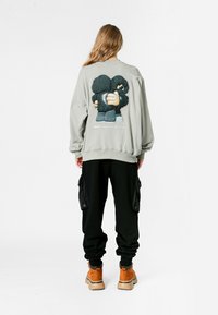 Sudadera de gran tamaño de color gris claro con un gráfico de dibujos animados en la parte posterior, combinada con pantalones cargo negros y botas color marrón.