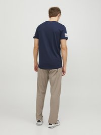 Mørkeblå T-shirt med korte ærmer og hvide striber på ærmerne, parret med lyse beige bukser og sneakers, vist fra bagsiden.