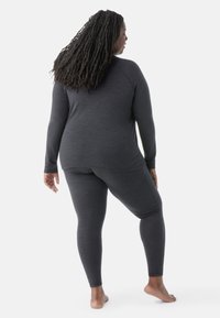 Mørkegrå termotøjssæt bestående af en langærmet bluse med rund kant og tætsiddende leggings, lavet af blødt, struktureret stof.
