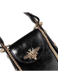 Zwarte nep lederen schoudertas met een gouden bij-embleem, kettingband en gestudde details aan de zijkanten. Zachte, glanzende textuur.