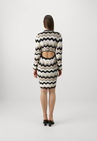 Robe en tricot avec un motif chevron en crème, beige et noir. Manches longues et découpe dans le dos. Silhouette ajustée avec un ourlet au-dessus du genou.