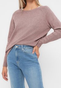 Hellrosa gestrickter Pullover mit rundem Halsausschnitt und gerippten Bündchen, kombiniert mit hellblauen Denim-Jeans in klassischer Passform und fünf Taschen.